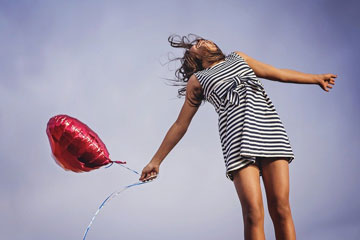 girl holding a red balloon and jumping in the air.